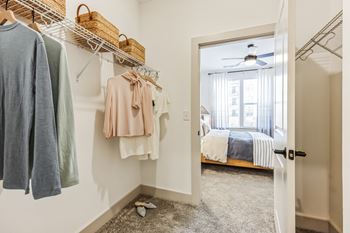 A walk in closet with clothes hanging on a rack and a door to a bedroom